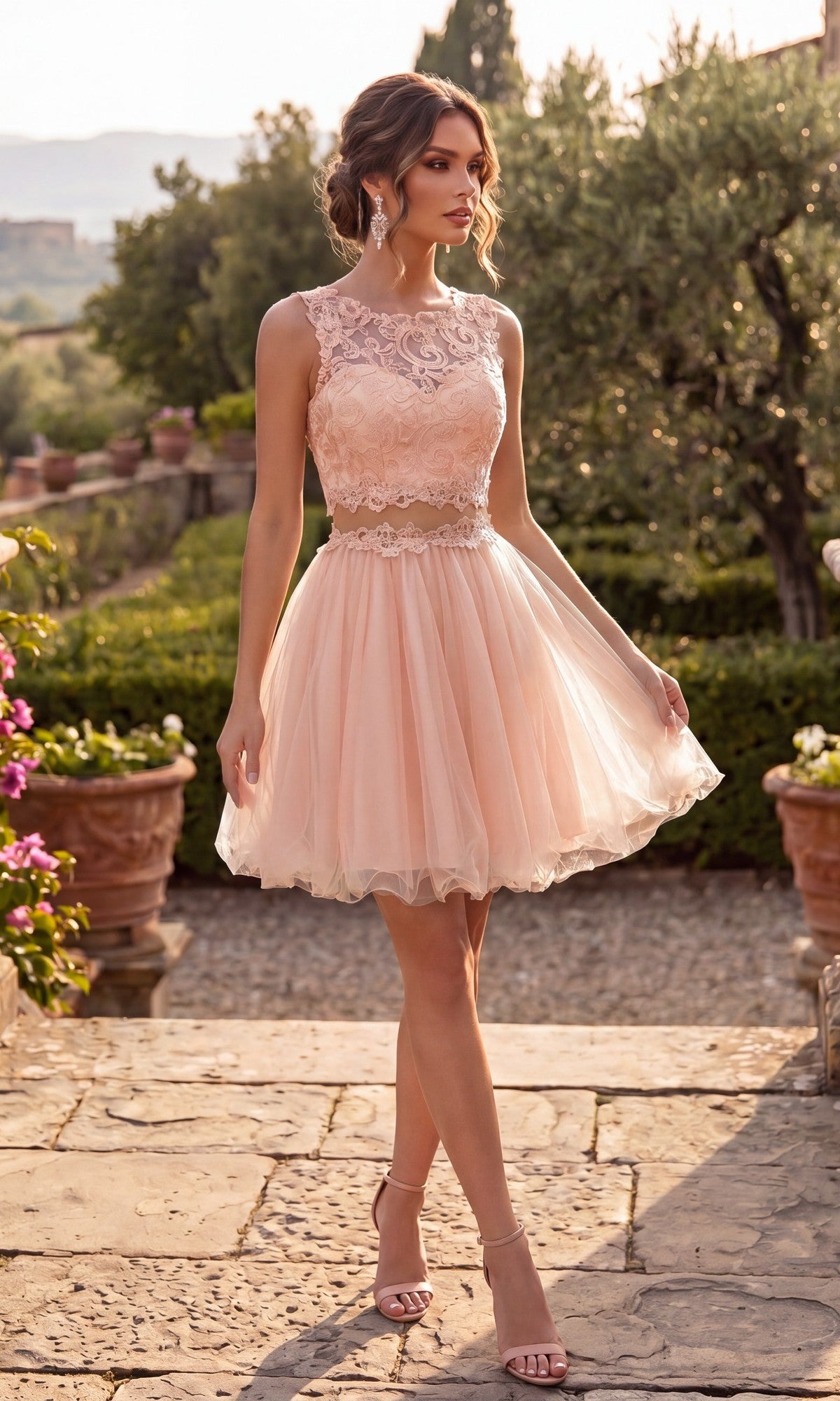 A woman stands outdoors on a stone path surrounded by greenery and potted plants, wearing the Chicas C9350 short homecoming dress in blush—a sleeveless, knee-length design featuring an illusion lace bodice and a flowing a-line tulle skirt.